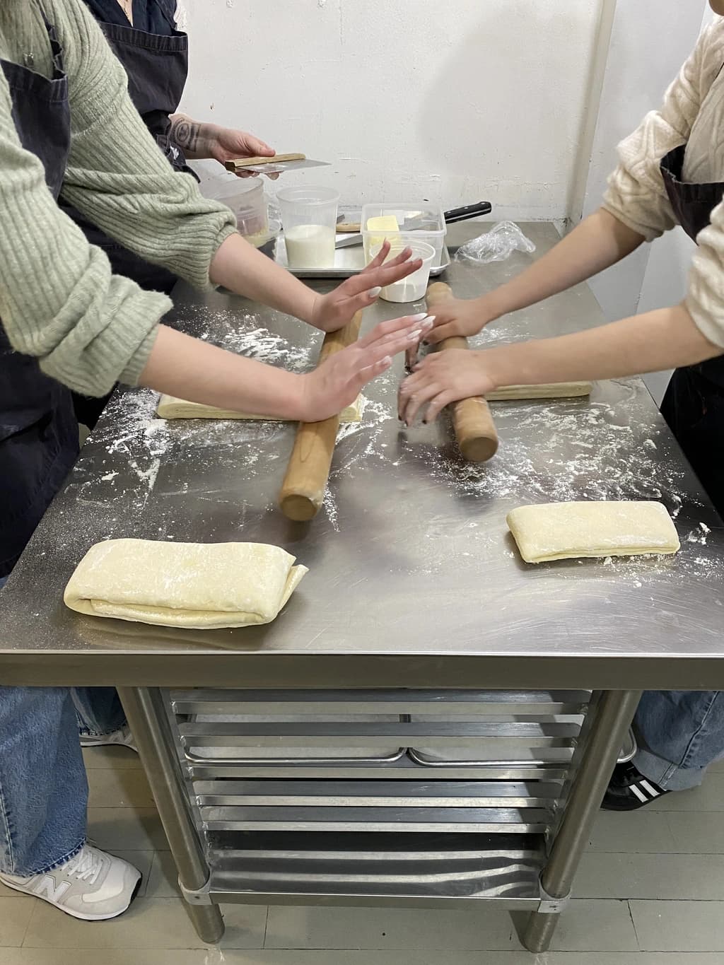 People rolling dough with rolling pins on a flour-covered table, preparing pastries.