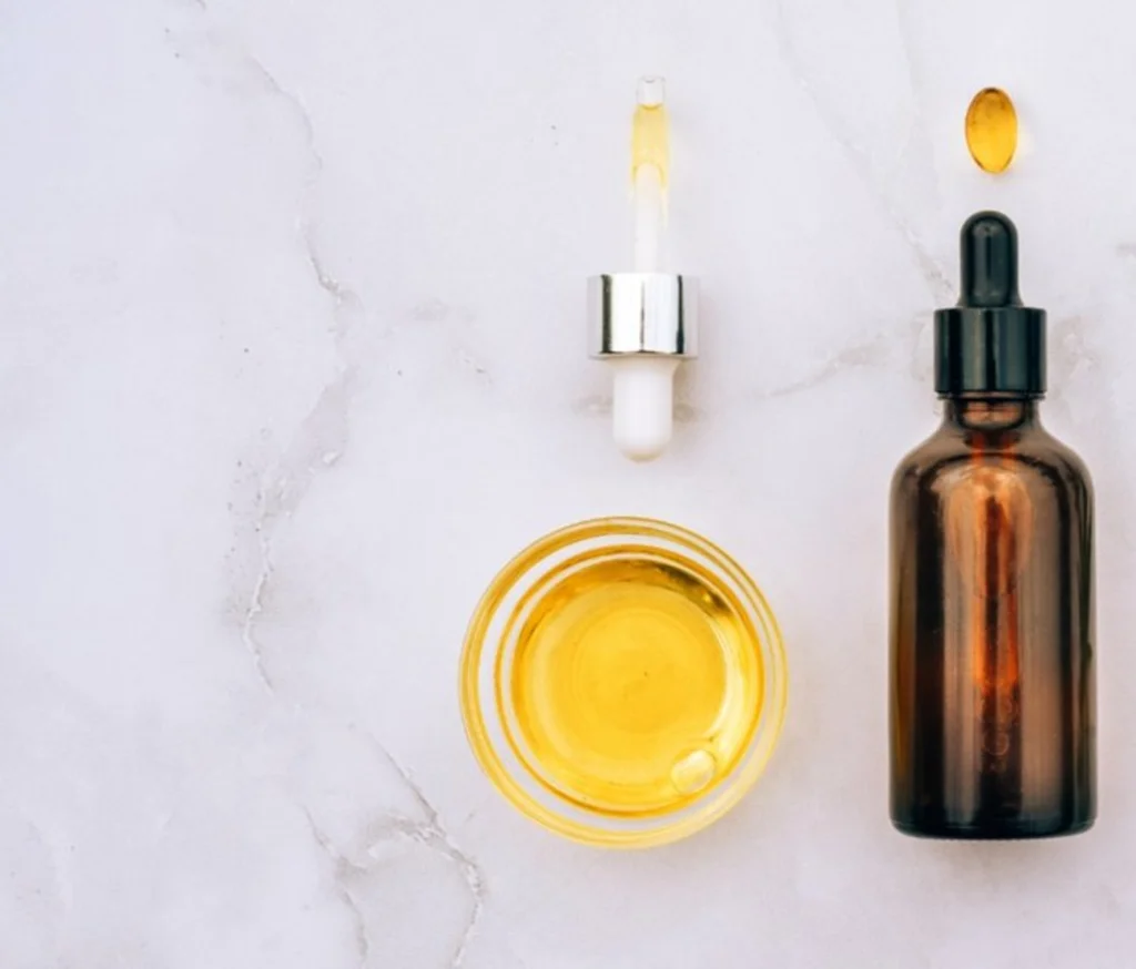 A dropper bottle of herbal tincture on a marble surface with golden oil in a glass dish.
