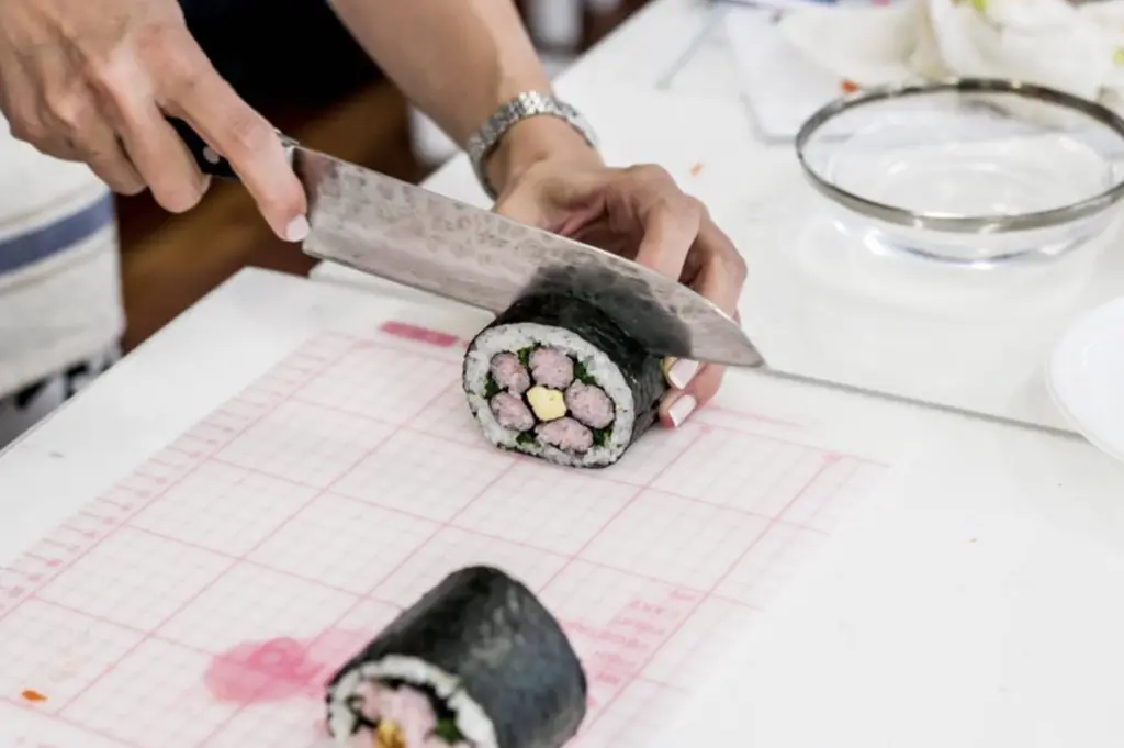 somenone cutting a sushi roll with a flower in the middle