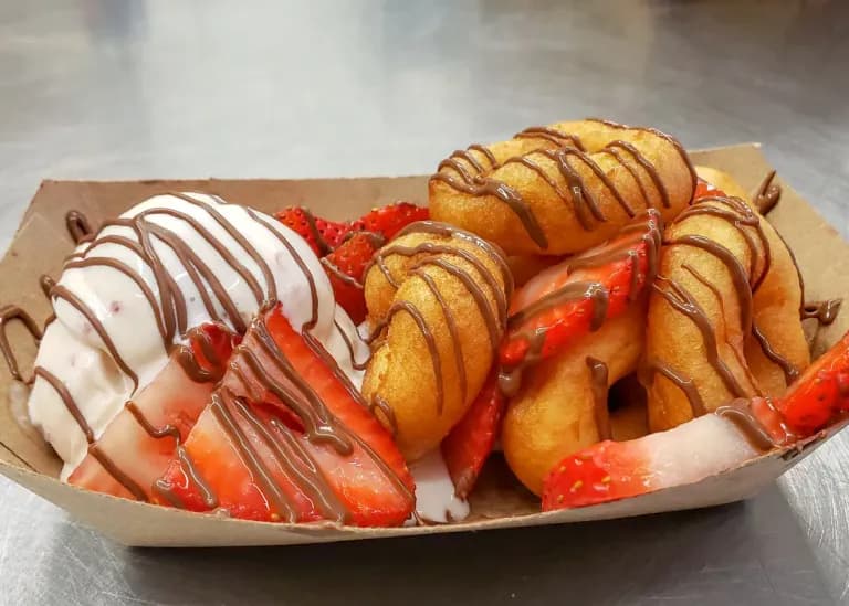 close-up of a dessert tray with mini donuts, sliced strawberries, and a scoop of vanilla ice cream, all drizzled with chocolate sauce.