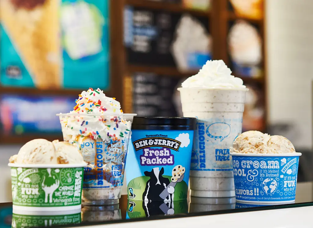 A variety of Ben & Jerry's ice cream treats, including scoops in cups, a milkshake topped with whipped cream and sprinkles, and a pint of Fresh Packed ice cream.