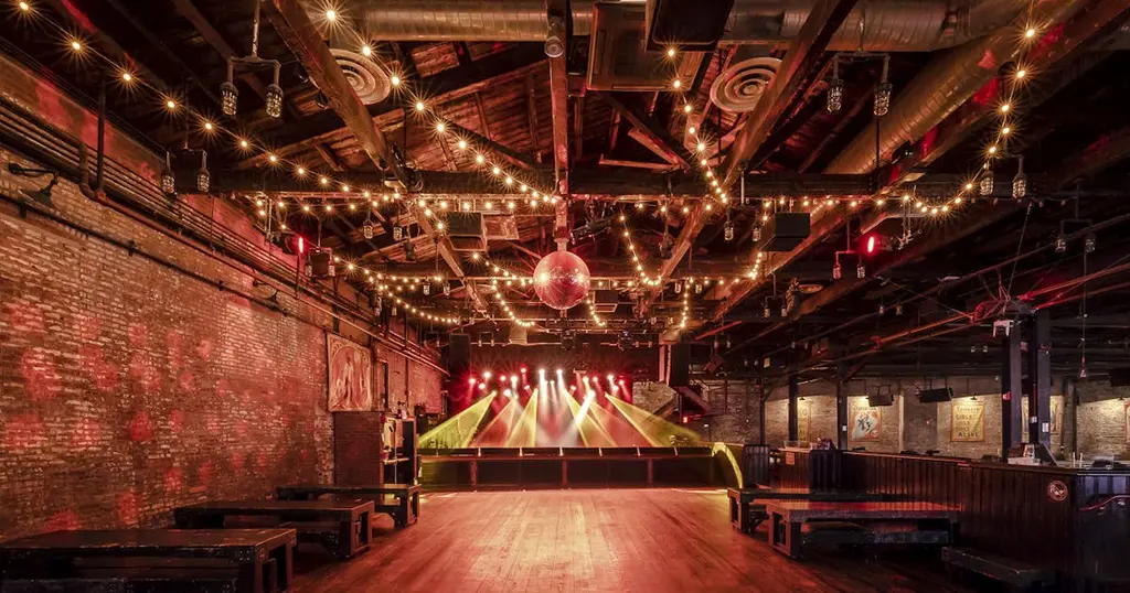 Spacious event venue with string lights, a disco ball, and a stage with lighting, perfect for concerts and large gatherings.