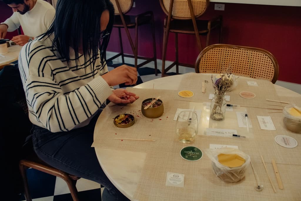a person making a candle at a table with supplies around them