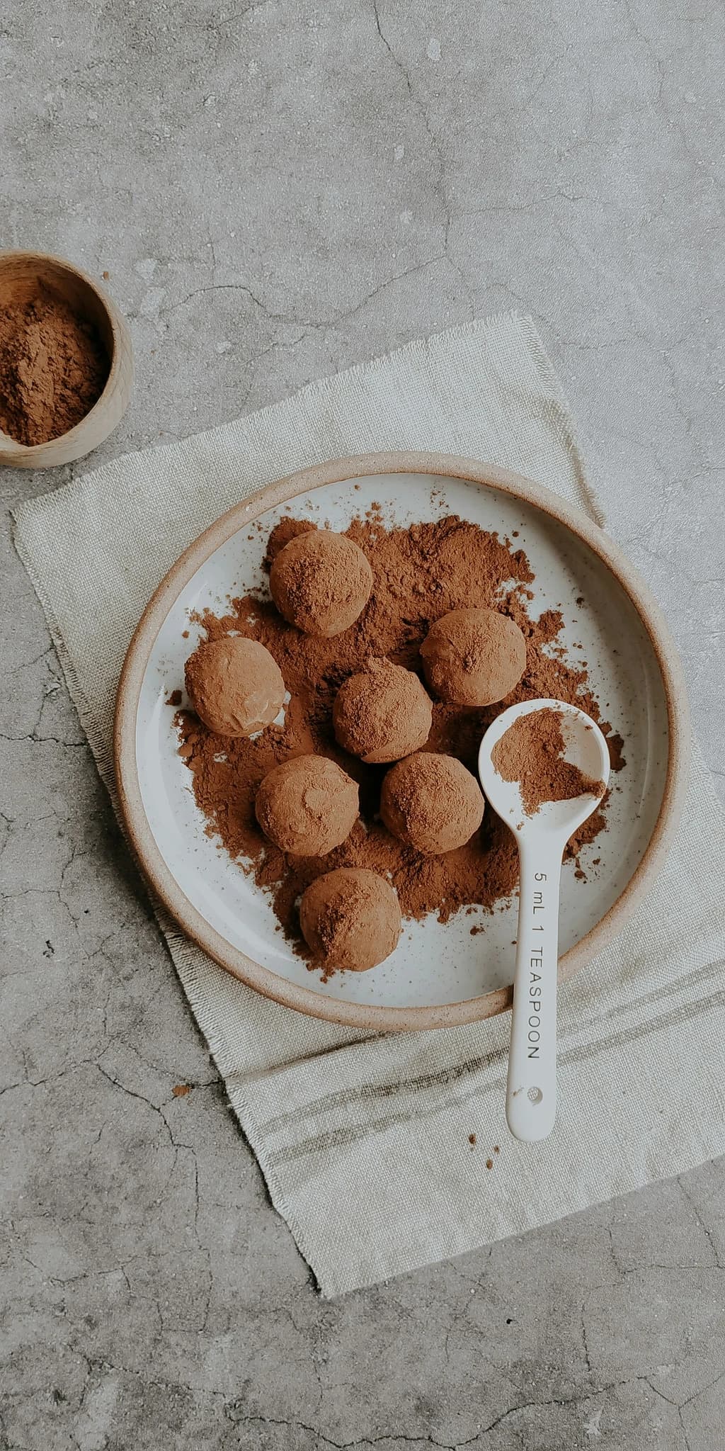 Plate of cocoa-dusted chocolate truffles with a teaspoon of cocoa powder beside them on a rustic surface.