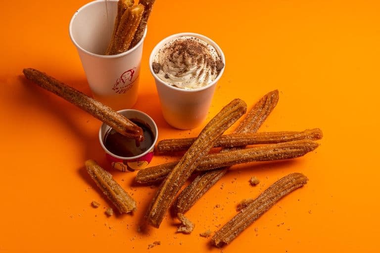 Churros with chocolate sauce and whipped-cream drink on an orange background.