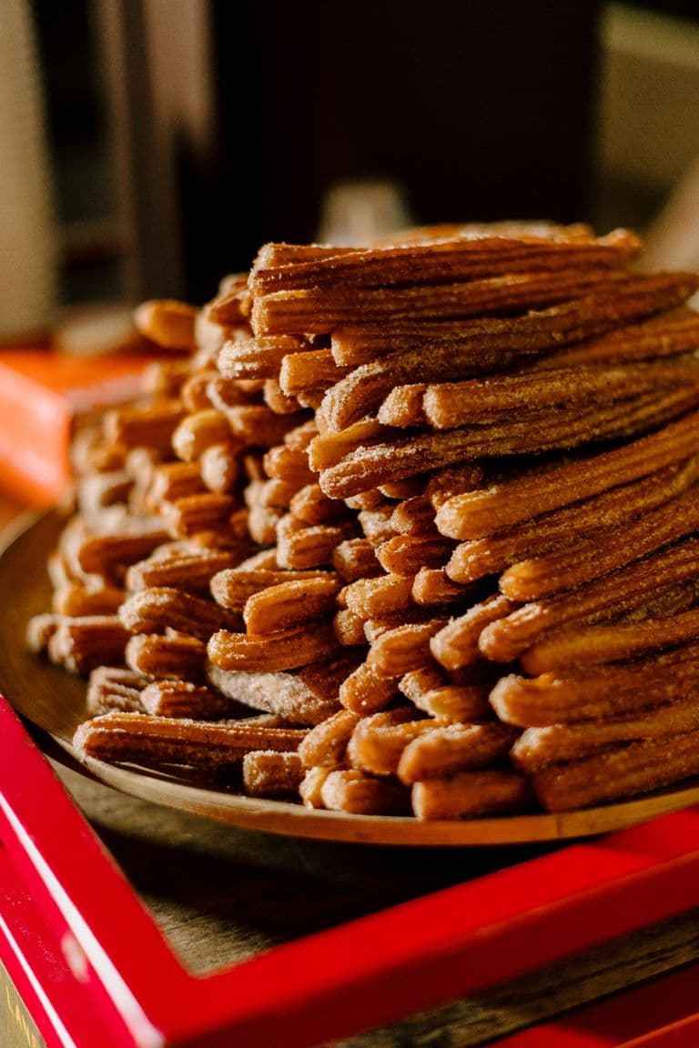 Large pile of cinnamon-sugar churros stacked on a plate.