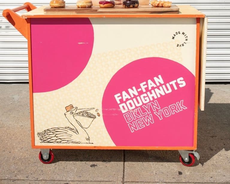 Smiling vendor standing behind cart with donuts arranged on top.