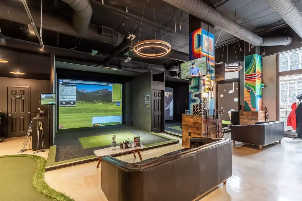 a golf simulator with coaches and coffee tabels behind them