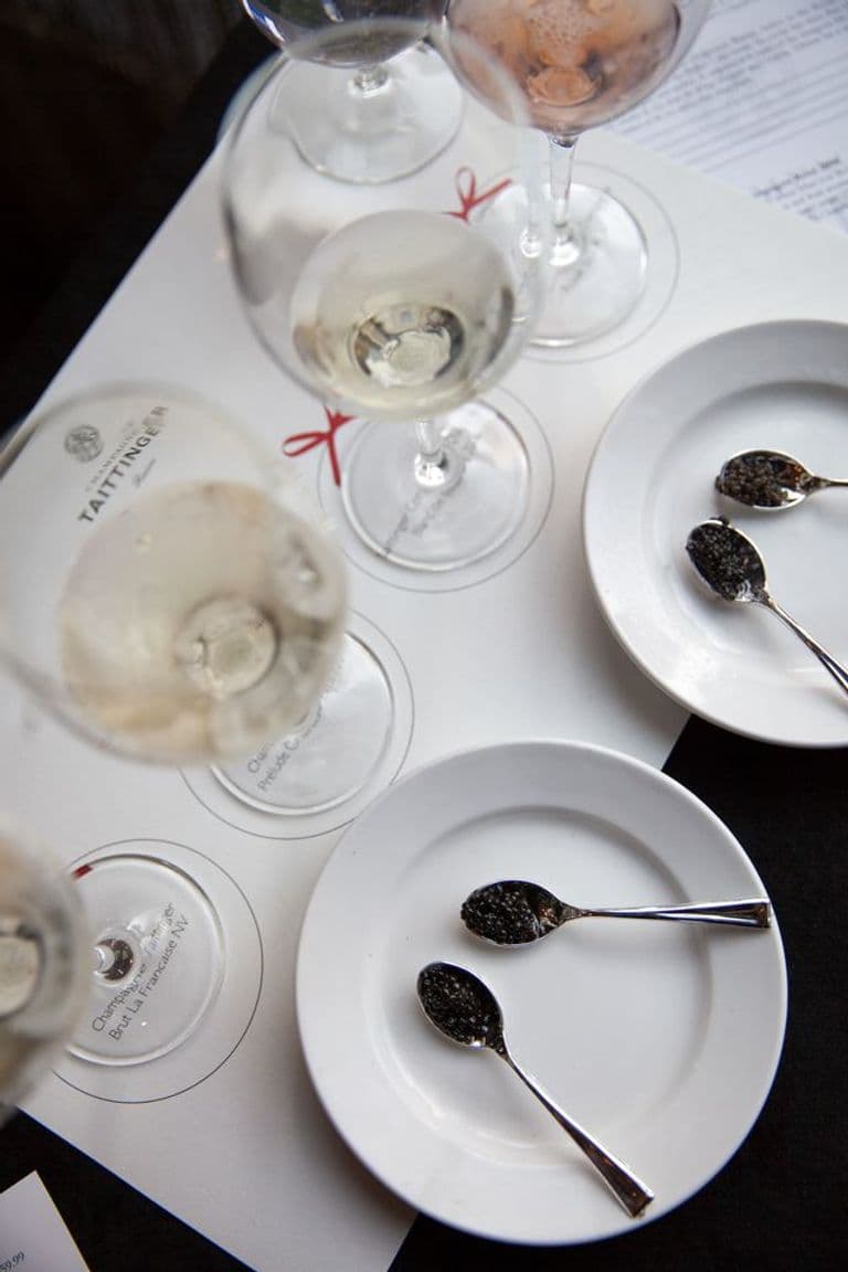 Tasting setup with spoons of black caviar on white plates paired with glasses of sparkling wine and champagne