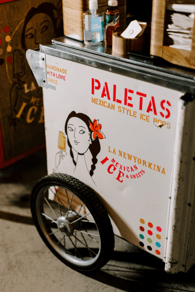 Paletas cart with colorful branding and wheels, set up to serve Mexican-style ice pops at an event.