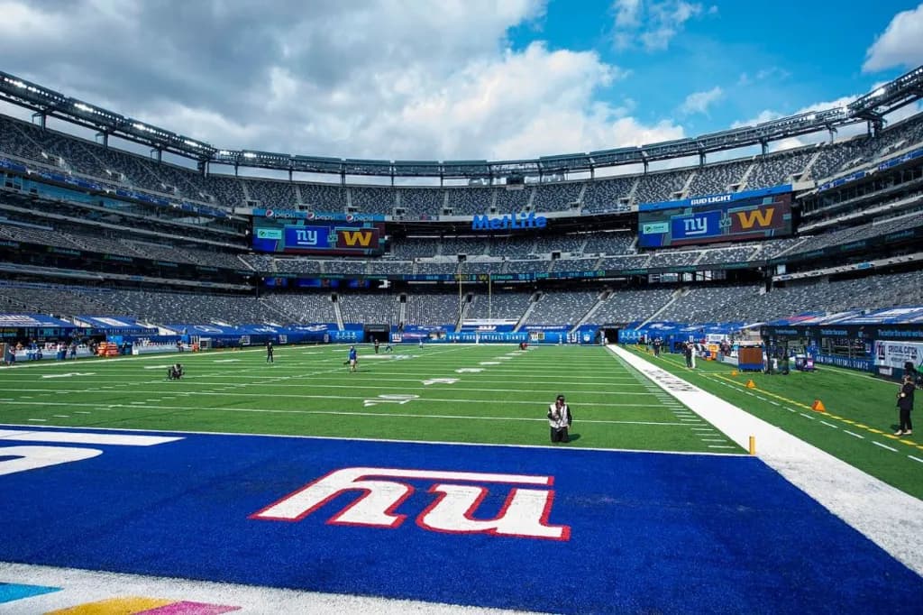 View of MetLife Stadium's field from the end zone, featuring the New York Giants branding and preparation for a game under a partly cloudy sky.