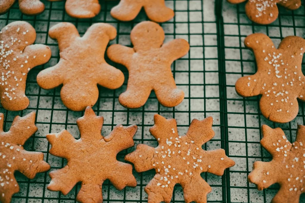 Close-up of gingerbread cookies in the shape of gingerbread men and snowflakes, cooling on a wire rack with light sugar sprinkle.