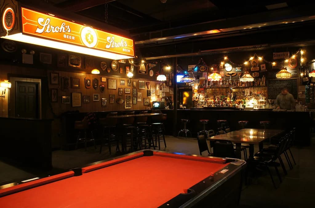 Cozy bar area with a vintage feel, featuring a pool table, warm lighting, and a well-stocked bar with various drinks.