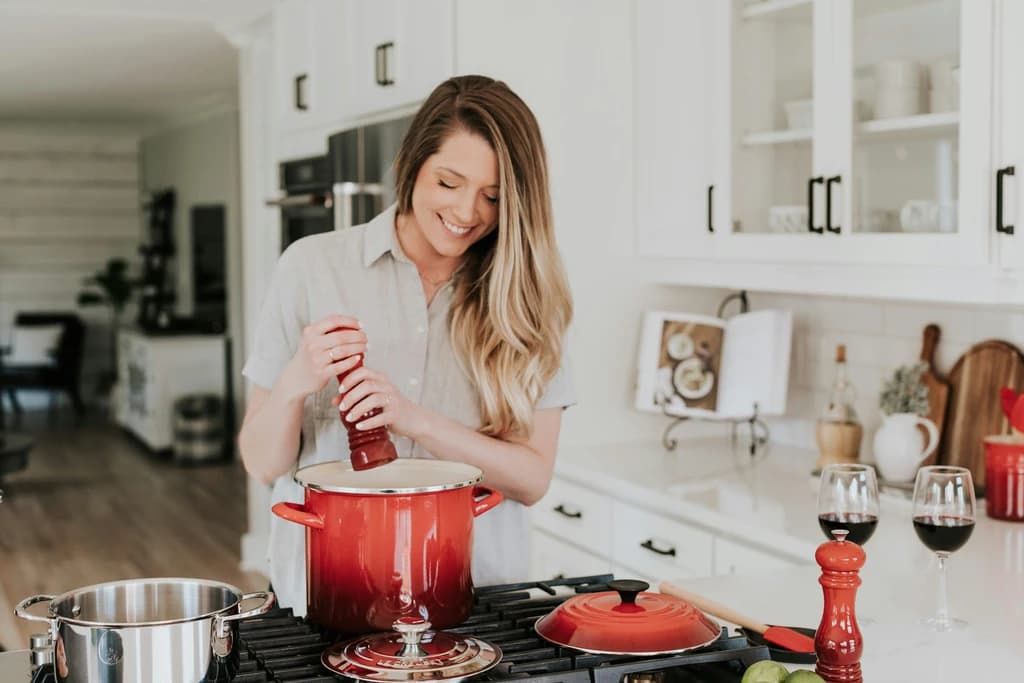 a women putting spices into a large cooking pot on aa stove