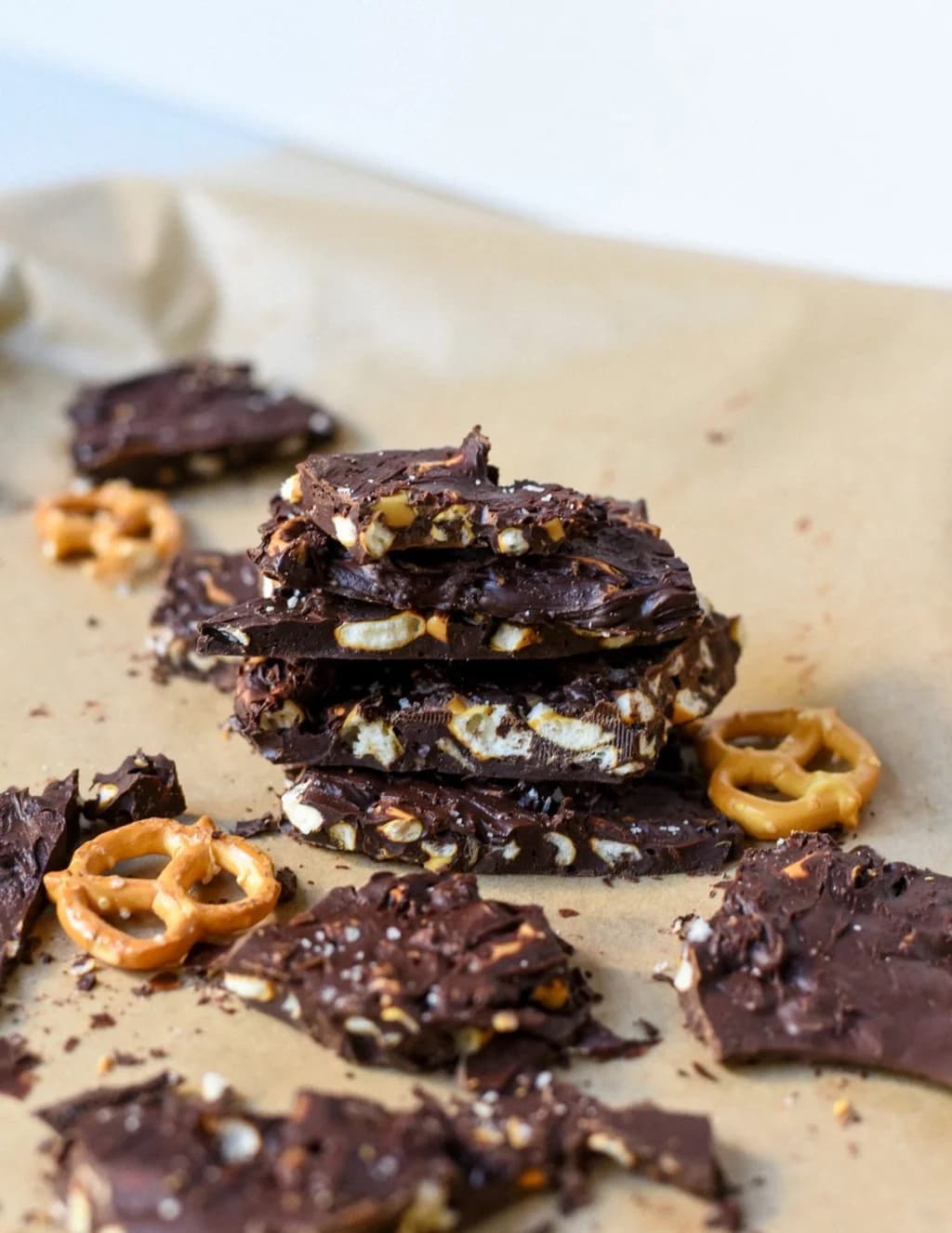 Stack of chocolate bark with pretzel pieces, resting on parchment paper with scattered pretzels.