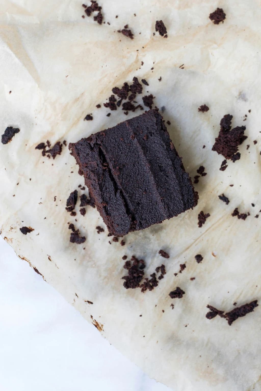 A single chocolate brownie square with crumbs on parchment paper.