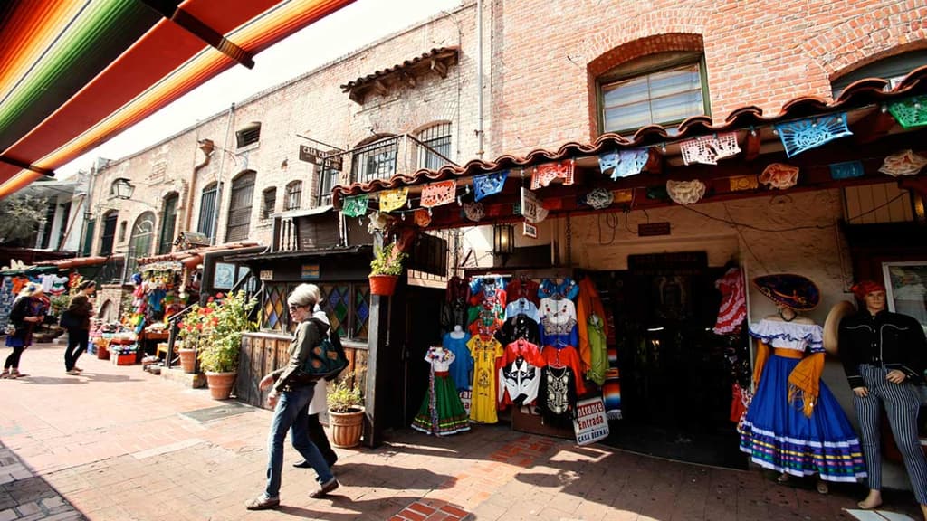 Colorful Mexican market with traditional clothing and decorations, under a canopy of vibrant stripes, set in a historic brick building setting.