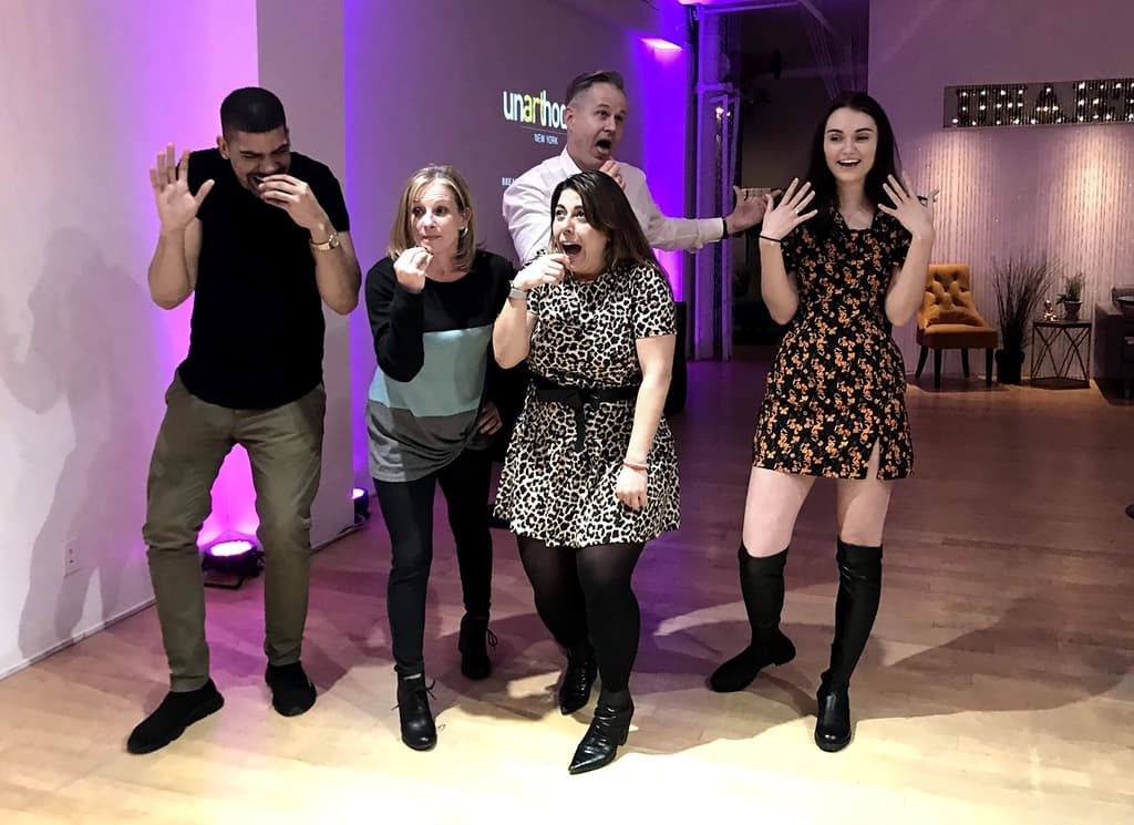 Six participants sitting and performing on stage, involved in an improv scene with dramatic gestures and lively expressions.