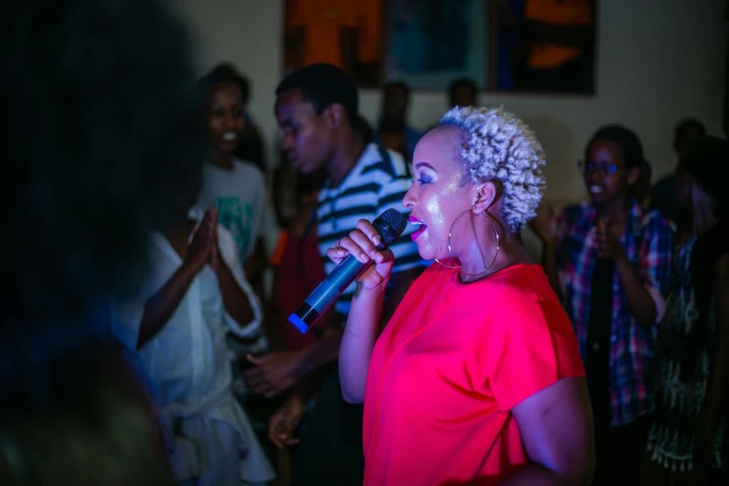 a women singing into a microphone in a dark room with people around
