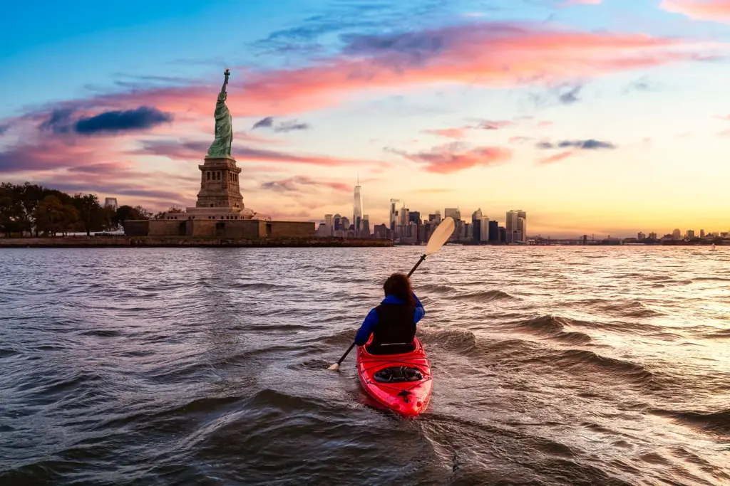 Someone kayaking in the Hudson River with the statue of liberty in the background