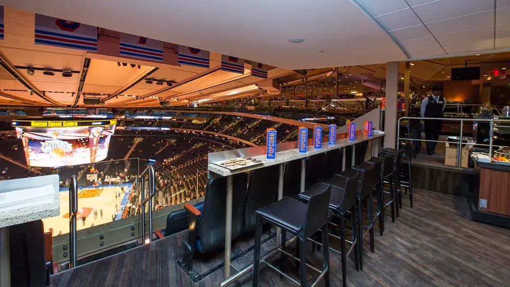 Luxury suite at Madison Square Garden with a view of the Knicks game, high-top seating, and a private dining area.