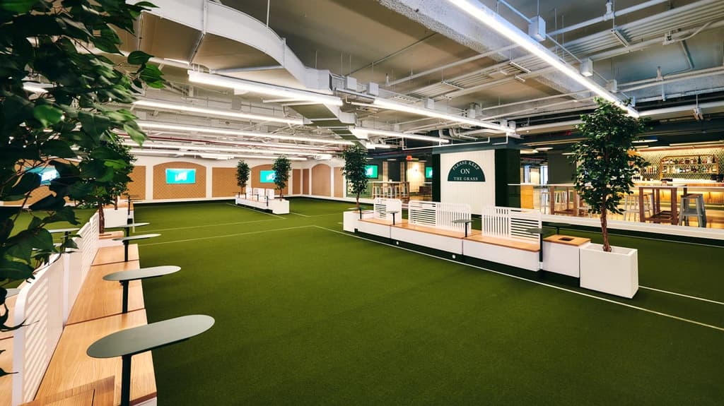 Indoor recreational space with artificial grass, seating areas, and small tables, designed for lawn games.