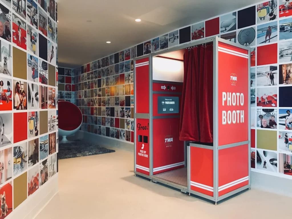 A retro red photo booth with a TWA hotel logo, surrounded by a photo-covered wall.