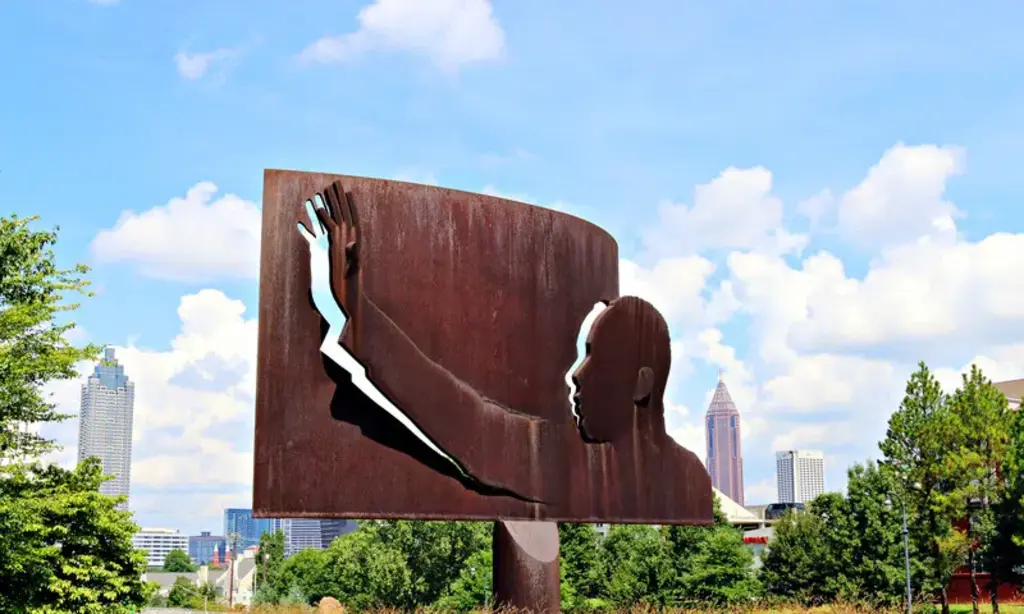 A metal sculpture of Martin Luther King Jr. with his hand raised, set against the Atlanta skyline and a clear blue sky.
