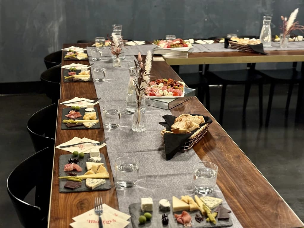 A close-up of a long table set for a cheese tasting, with plates of cheese samples, glasses of water, and bread baskets.
