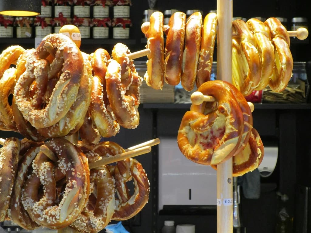 A display of freshly baked pretzels hanging on wooden sticks, some with salt and others with cheese, in a traditional market setting.