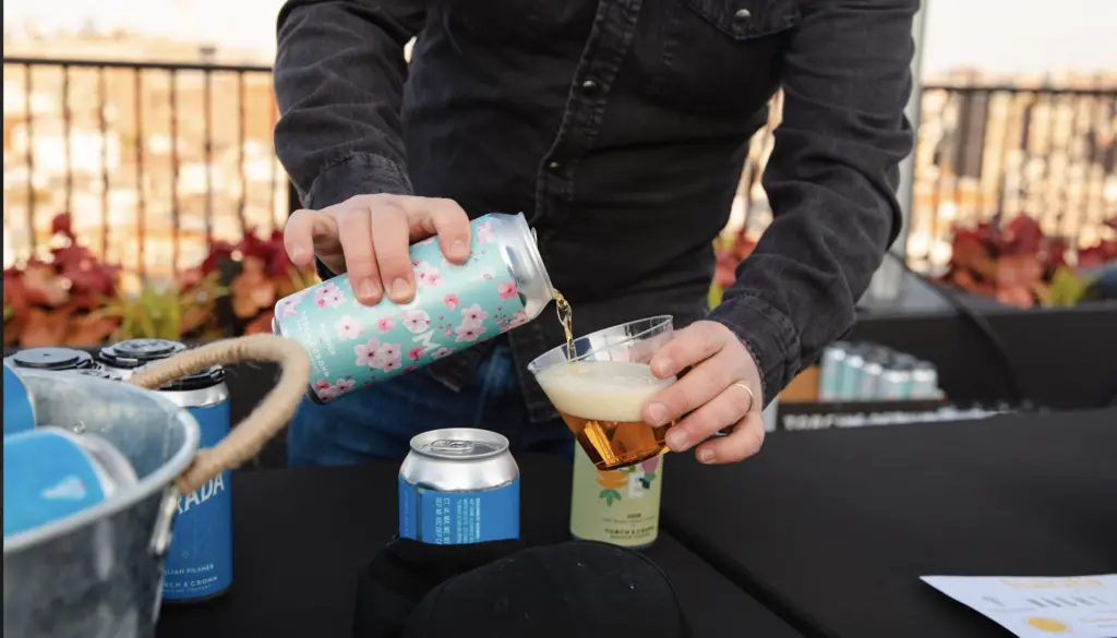 A person in a denim shirt pours a glass of beer from a tap.