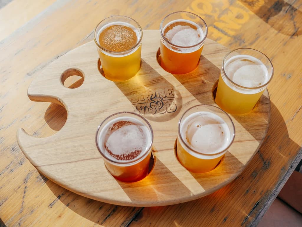 A wooden tasting board with six glasses of beer, each filled with different shades of golden to amber hues, ready for sampling.