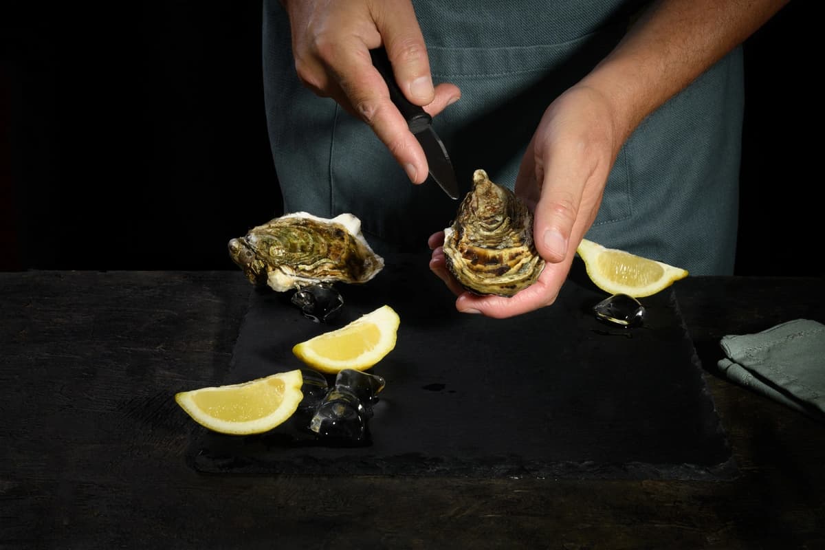 Opened oysters and lemon on a rustic wooden surface with a burlap cloth and oyster knife.