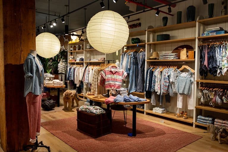 Faherty retail space with blue carpet, warm wood finishes, surfboard wall decor, and organized clothing displays for a relaxed and modern shopping environment.