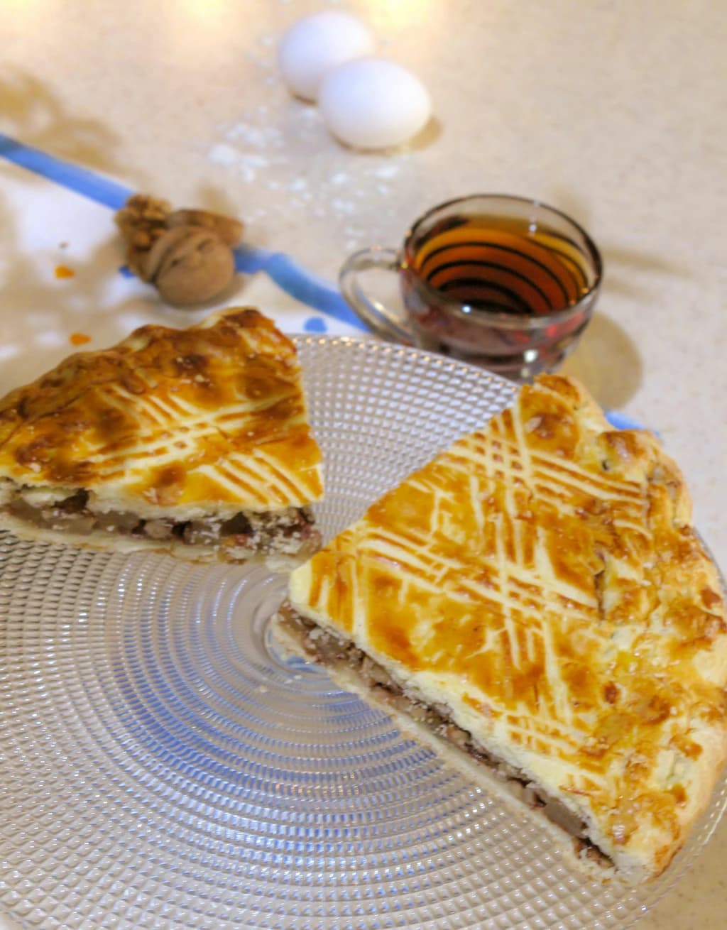 Two slices of a beautifully baked pie with a lattice design, accompanied by a cup of tea in the background.