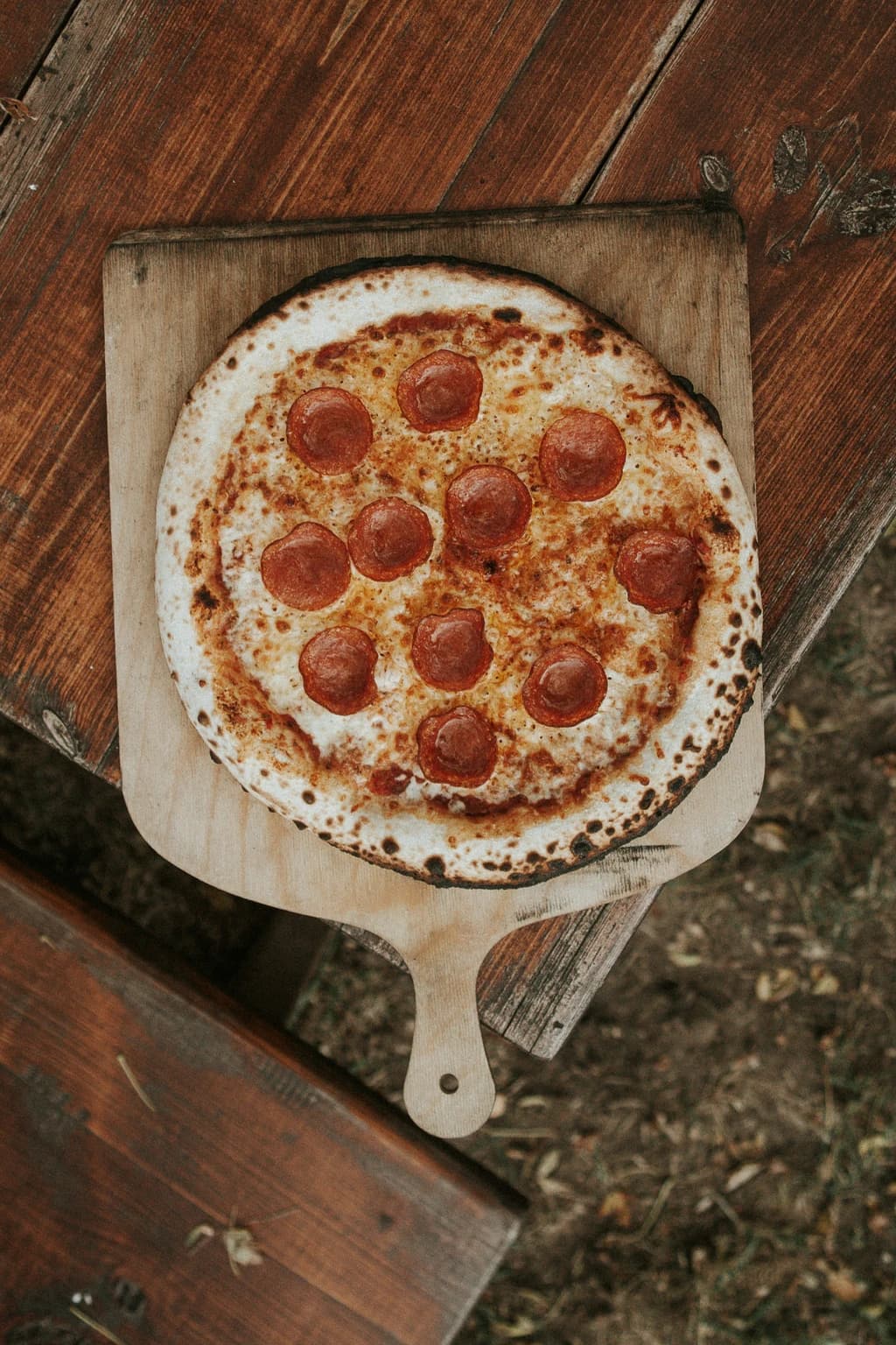 A freshly cooked pepperoni pizza on a wooden pizza peel, placed on a rustic wooden table.