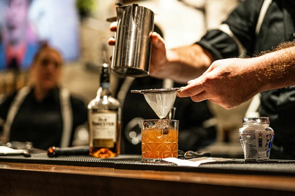 Close-up of hands pouring and straining a cocktail with bartending tools