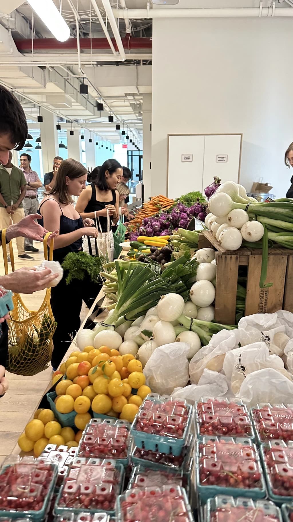 a large table with various produce on it and people selecting items from it