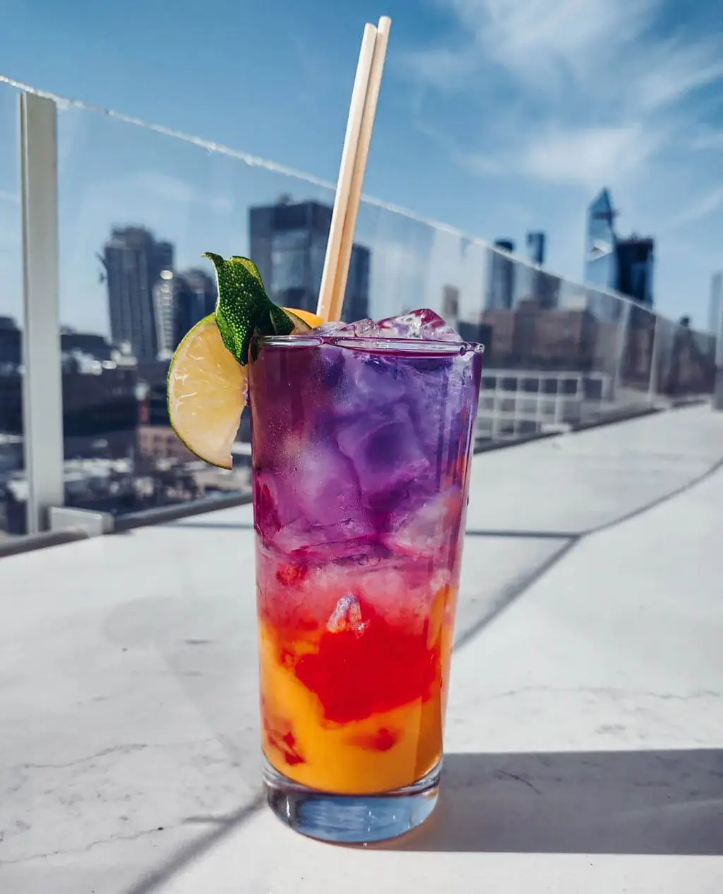 a cocktail with different colored layers in a glass with the new york skyline in the background