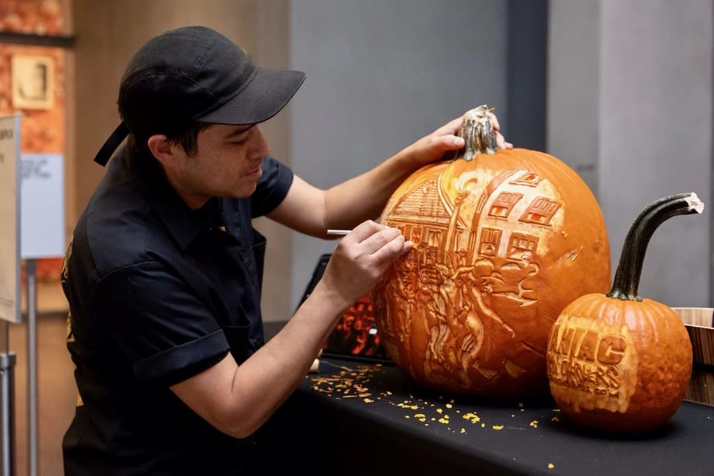 An intricately carved pumpkin with a haunted house and bats, featuring the text 'Happy Halloween,' glowing warmly in the dark.