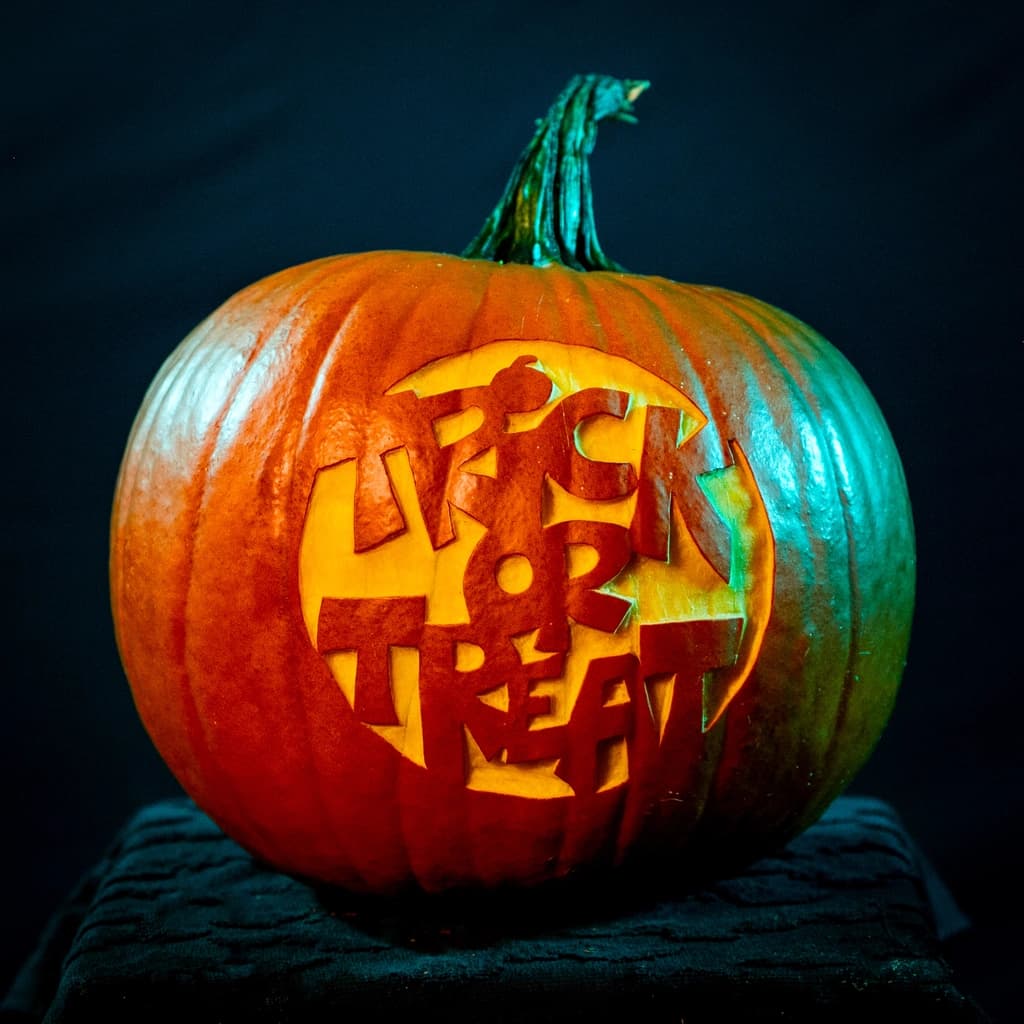 A pumpkin carved with the words 'Trick or Treat,' illuminated with soft lighting on a black backdrop.