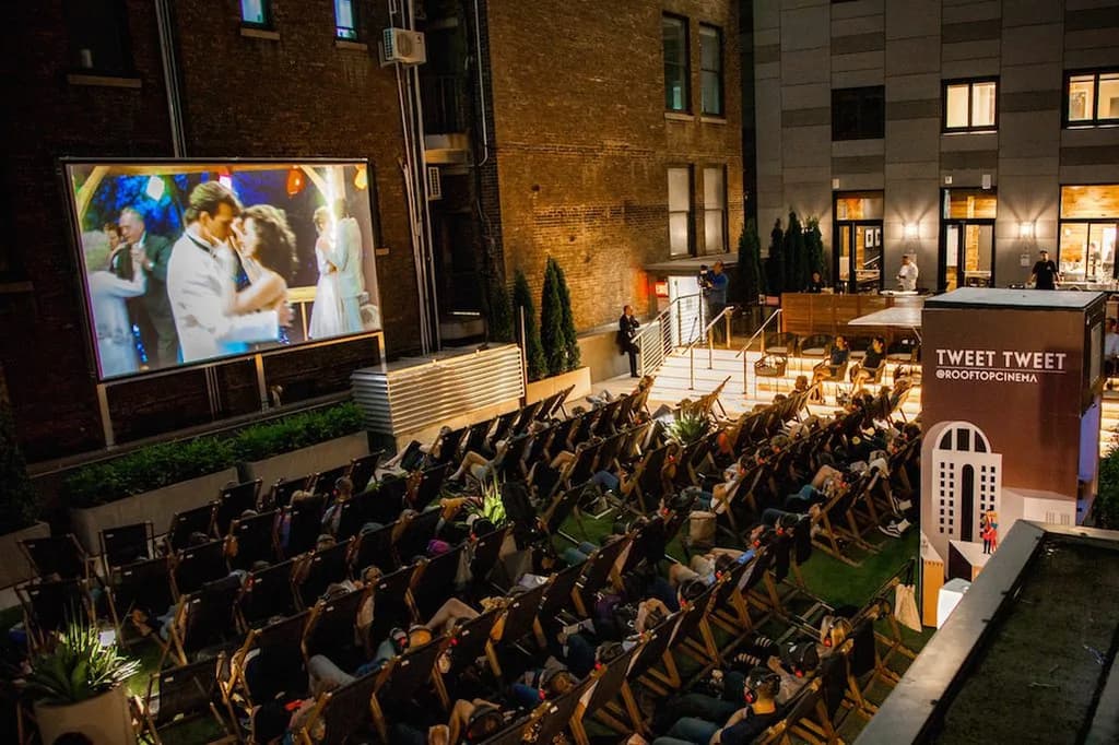 A rooftop cinema with people in lounge chairs watching a movie under the night sky, creating a cozy and unique outdoor movie experience.