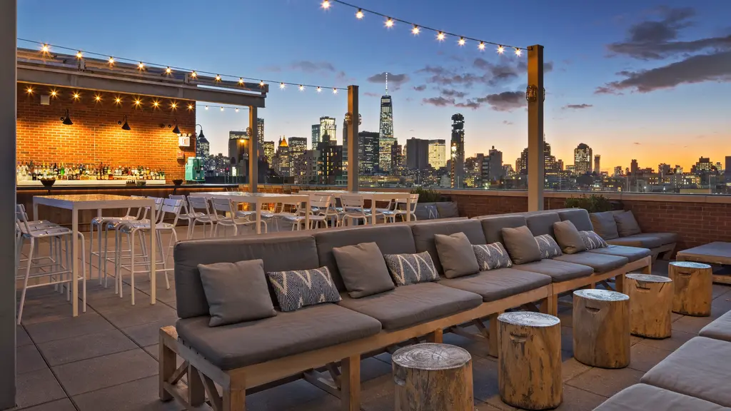 roof top bar with lounge seating, tables, and view of the city