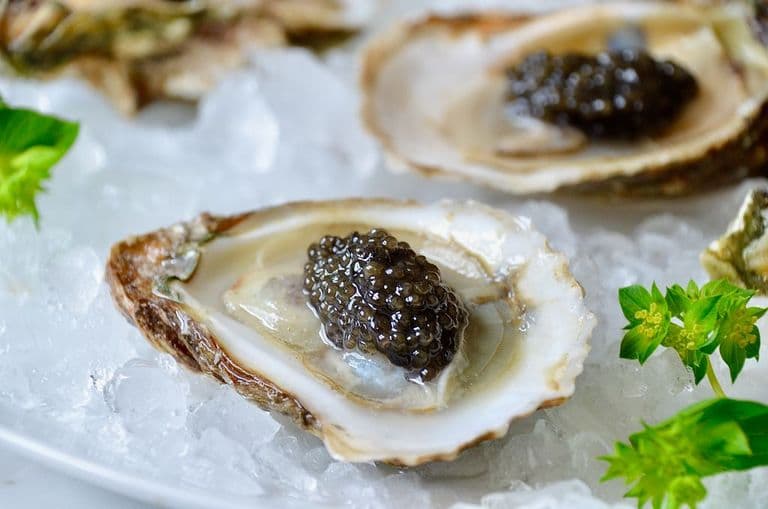 A fresh oyster on ice topped with a generous serving of black caviar, garnished with green herbs.
