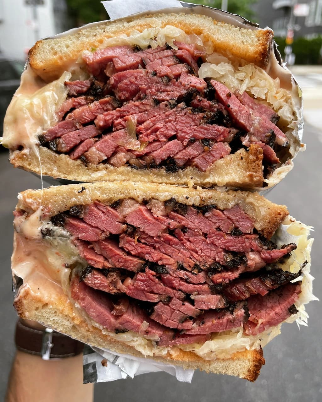 A pastrami sandwich cut in half, filled with tender, juicy meat and sauerkraut between crispy slices of bread.