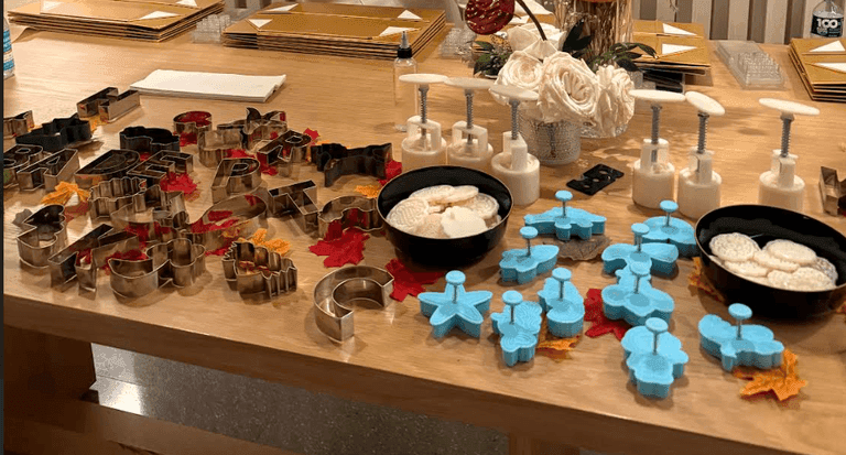A table set up for a cookie-making event with letter-shaped cookie cutters, decorative stamps, dough presses, and fall-themed decor.