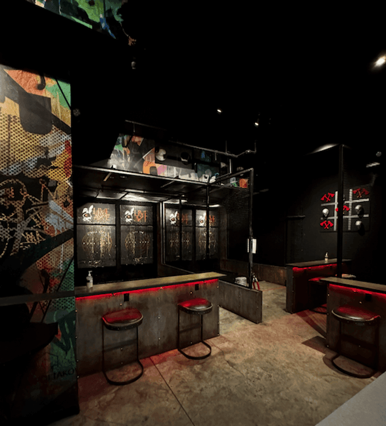 Multiple axe-throwing lanes and bar seating in a dimly lit venue with bold, colorful wall art.