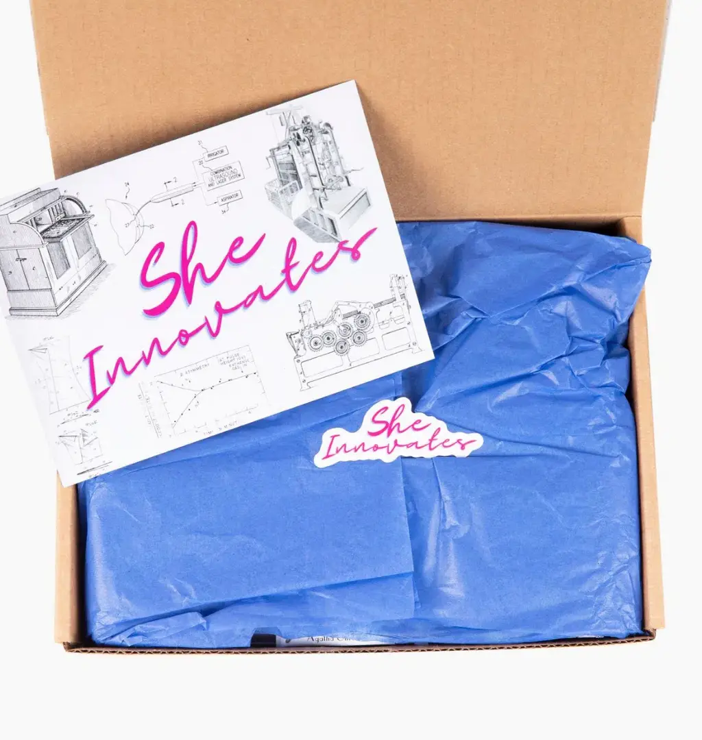 A subscription box with blue packaging, featuring an insert labeled 'She Innovates' alongside innovative tool drawings, promoting women in innovation.