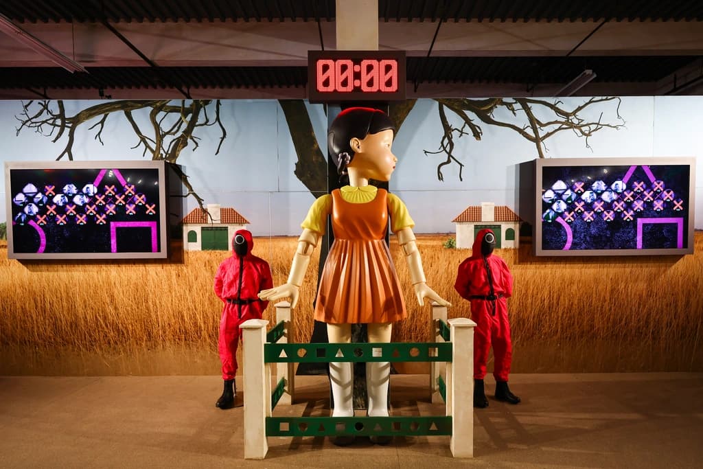 Squid Game-themed room featuring the giant robot girl from Red Light, Green Light, with pink-suited guards standing watch nearby.