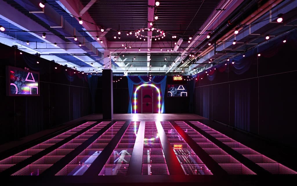 Squid Game room with neon-lit glass bridge challenge and vibrant entryway, creating an immersive experience true to the show’s tension.